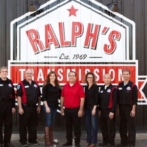 The team, dressed in black, stands in front of the large logo on the side of the building.