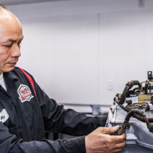 A Ralph's technician examines tubing and wiring for a vehicle.