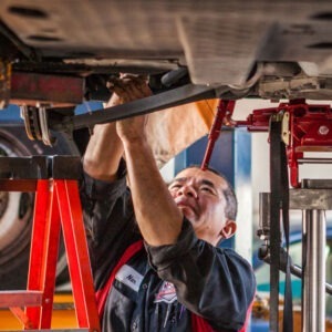 A man stands beside a ladder, working on the bottom of a car.