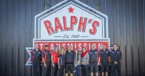 The Ralph's Technician team standing in front of a corrugated tin wall with the logo.