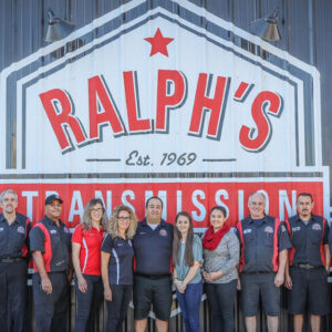The Ralph's Technician team standing in front of a corrugated tin wall with the logo.