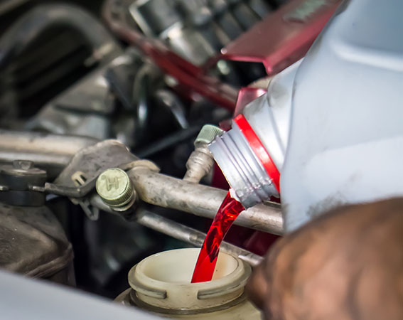 A silver bottle drips red liquid into a container in a vehicle.