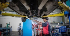 A man inserts a new part in the underbelly of a car.