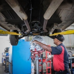 A man inserts a new part in the underbelly of a car.