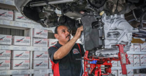A man works on the components of a car with it raised over his head.