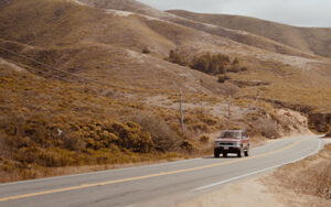 An older Ford vehicle driving through desert mountains.