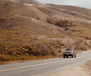 An older Ford vehicle driving through desert mountains.