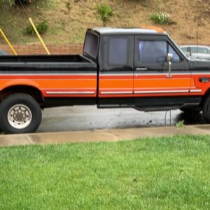 An image of a black and orange older Ford truck on a rainy day.