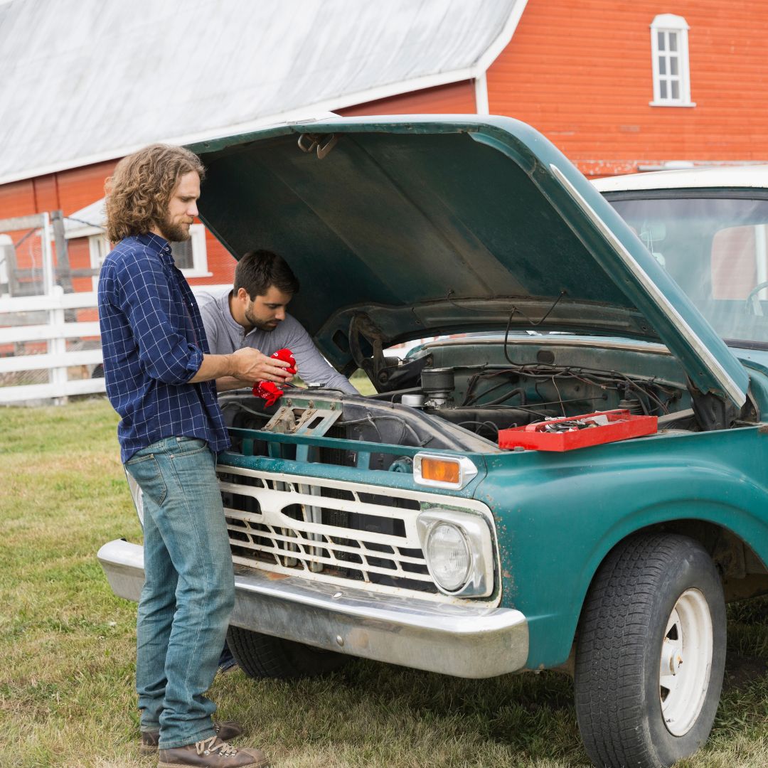 two men working on a truck at a farm